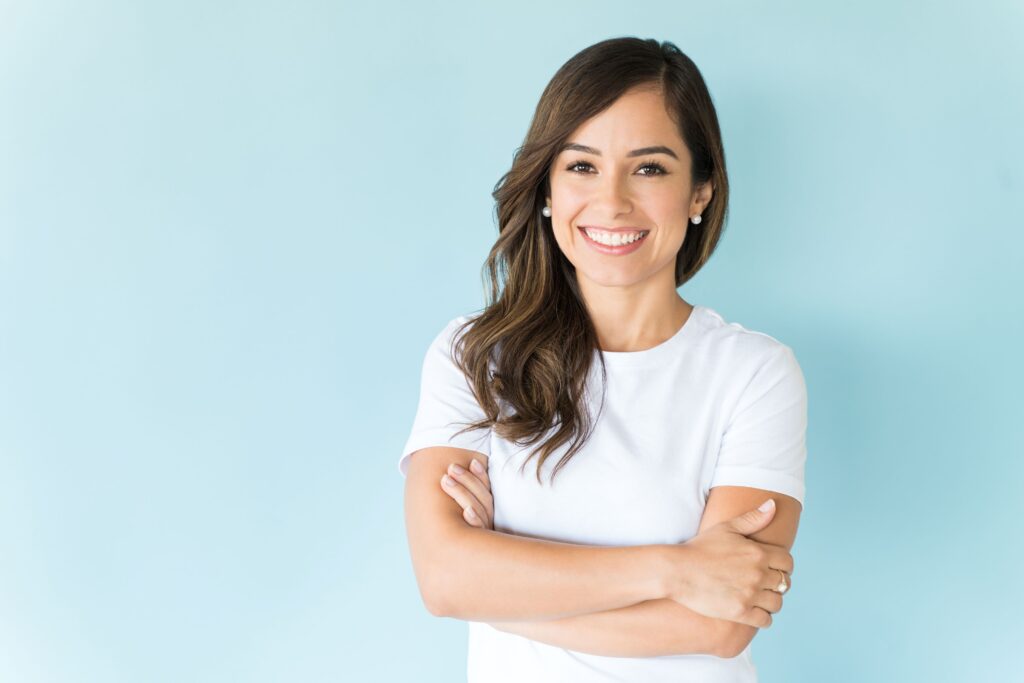 Woman with brown hair in white t-shirt smiling with light blue background